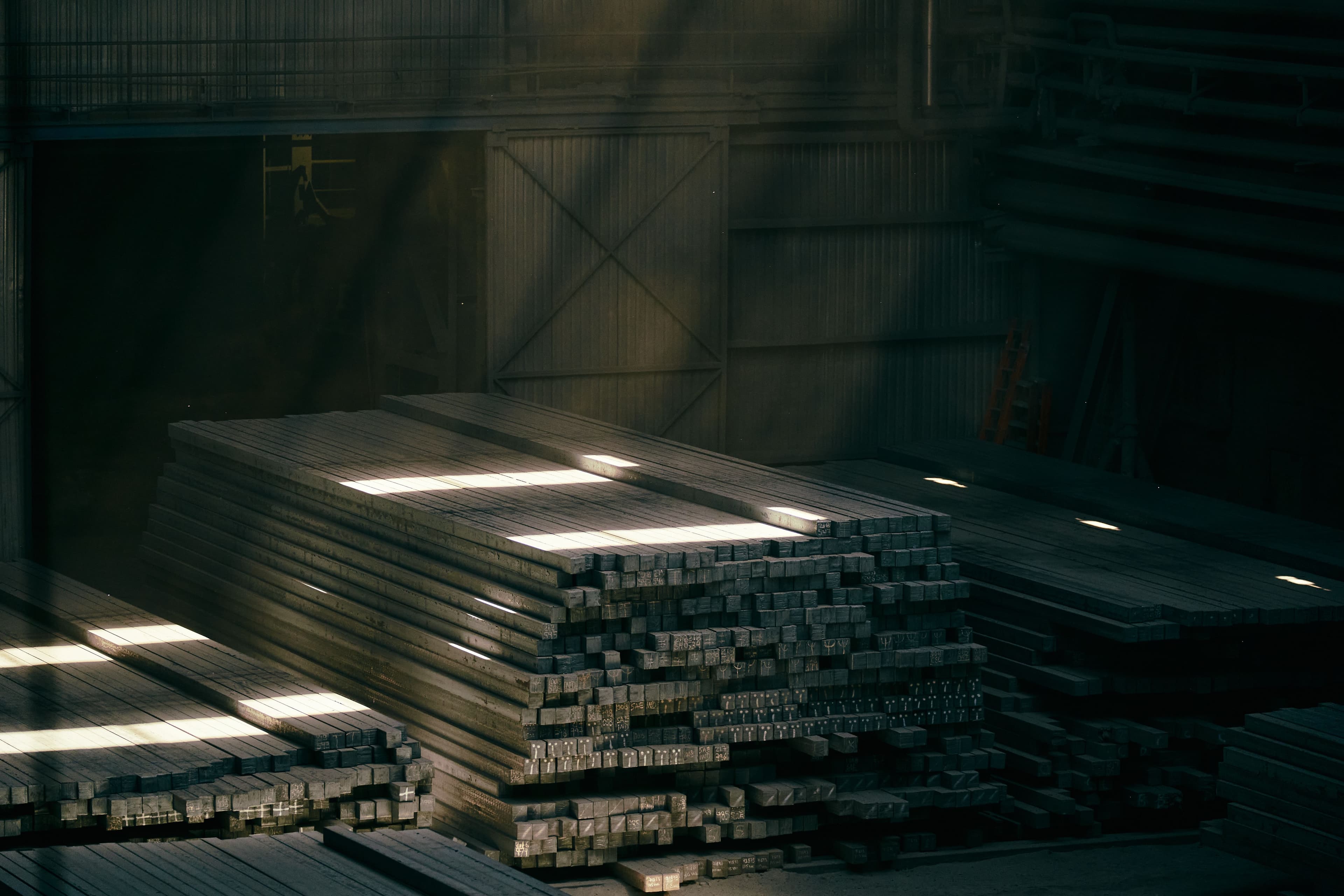 Stacked structural steel billets in a sunlit warehouse